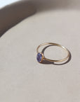 14k gold fill Purple rain ring placed on a white jewelry dish in the sunlight. This ring features a simple smooth band featuring a Tanzanite cab.