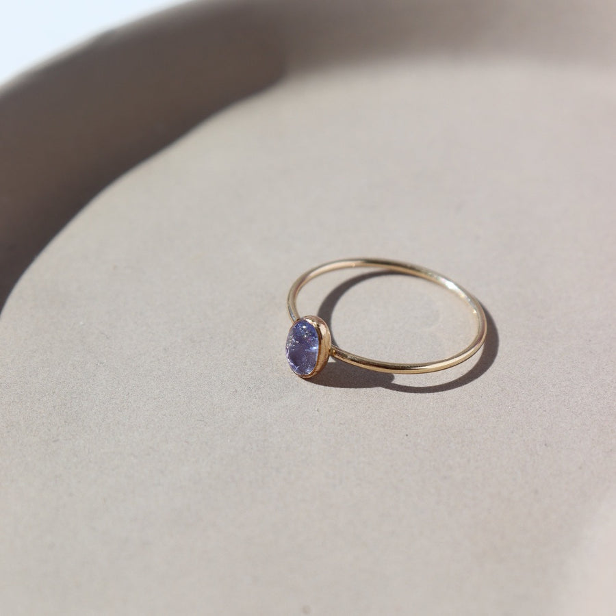 14k gold fill Purple rain ring placed on a white jewelry dish in the sunlight. This ring features a simple smooth band featuring a Tanzanite cab.