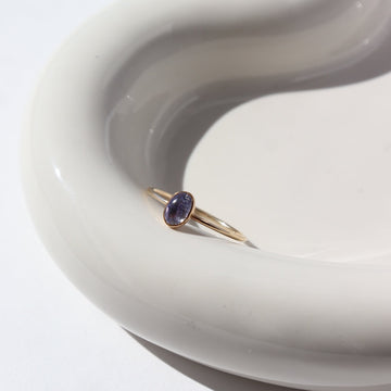 14k gold fill Tanzanite ring placed on a white jewelry dish in the sunlight. This ring features a simple smooth band featuring a Tanzanite cab.