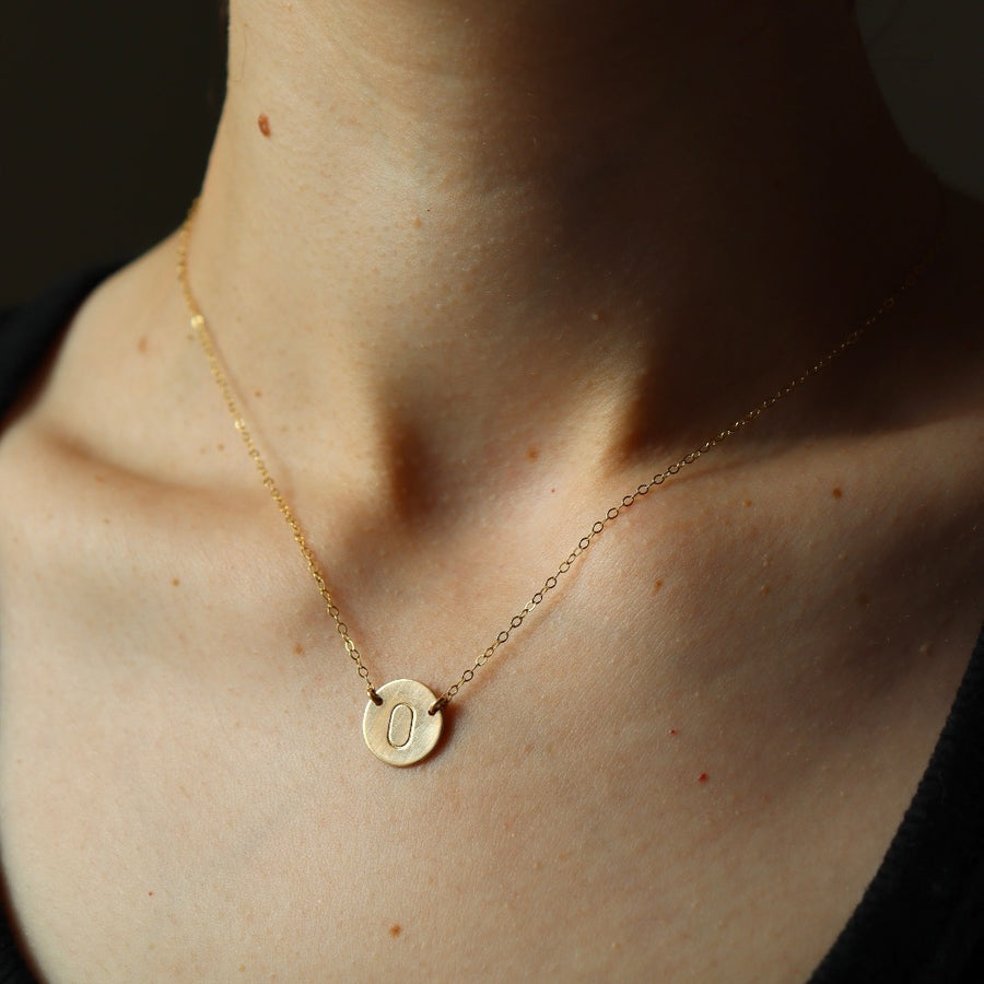 Model wearing a 16" 14k gold fill Anchored Initial Necklace with the initial "O" stamped on the coin pendent.