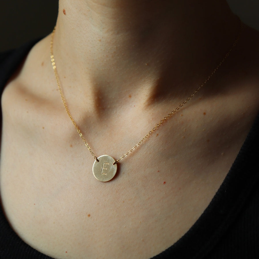 Model wearing a 16" 14k gold fill Anchored Initial Necklace with the initial "E" stamped on the coin pendent.