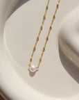 14k gold fill Beaded pearl necklace laid on a white plate in the sunlight. 