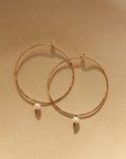 14k gold fill Emma pearl hoops laid on a tan plate in the sunlight