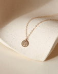 Gold filled necklace with a round hand stamped four leaf clover pendant on a beige stone surface