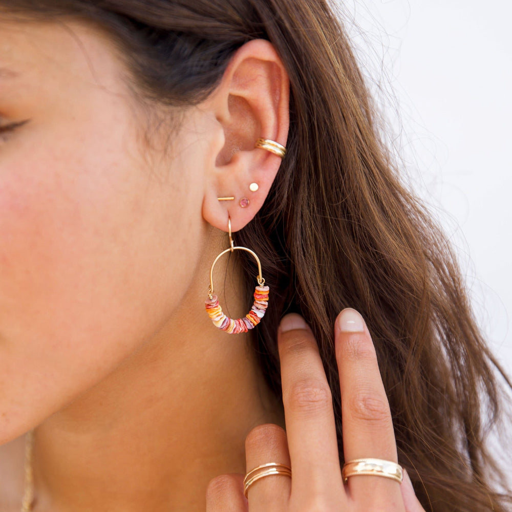 Gold hoop earrings with colorful beads on a beige background taken on a model