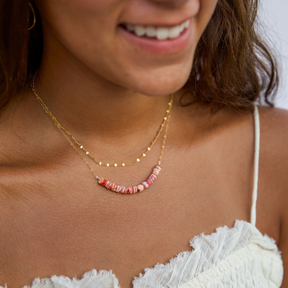 Close-up of a woman wearing a gold necklace with pink beads, smiling.