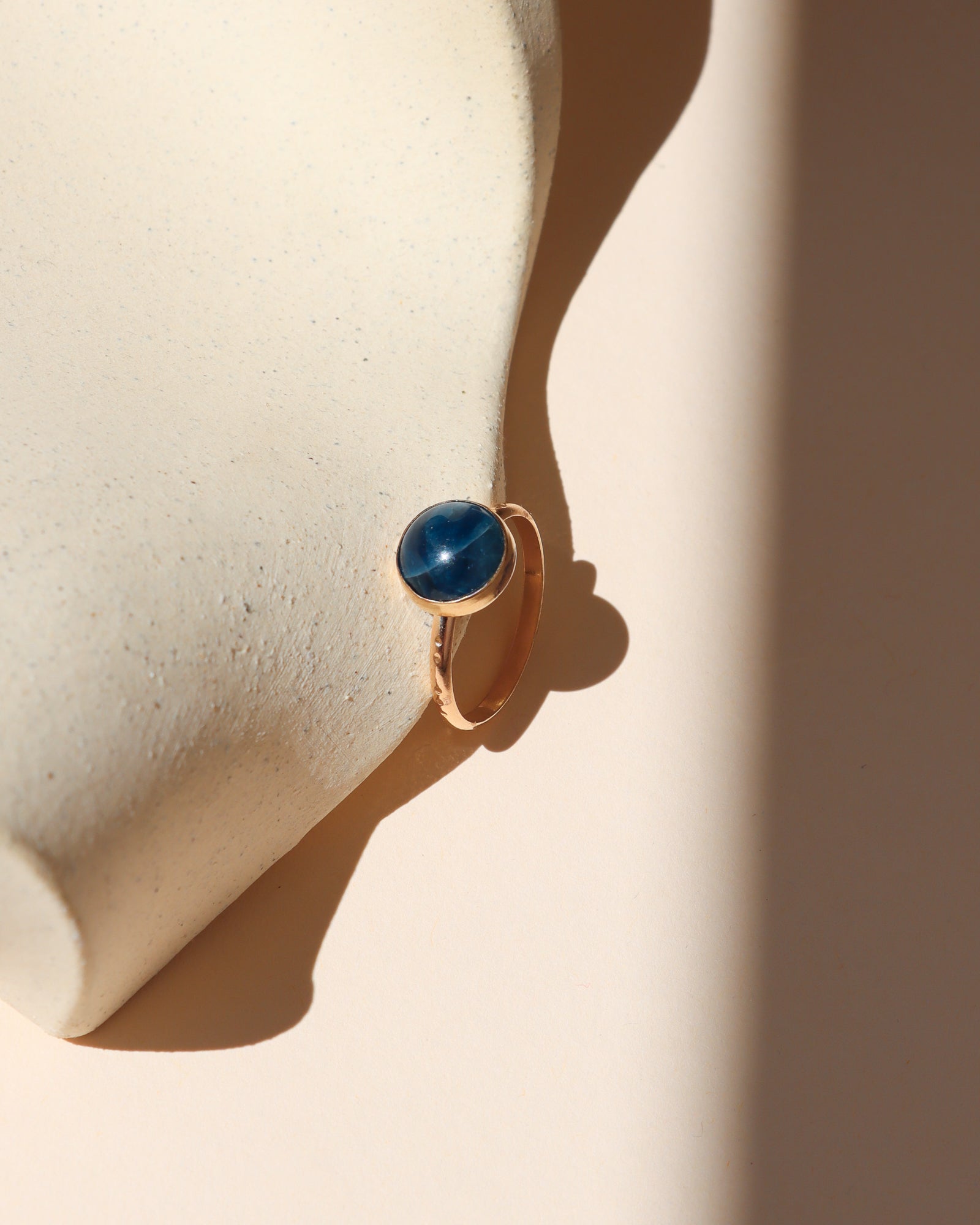14k gold fill ring with round blue stone on a light dish