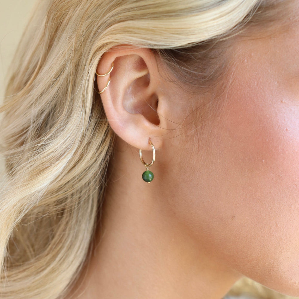 Model wearing 14k gold fill 14mm hoop with a Jade ball gemstone dangling from it. 