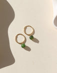 A 14k gold fill 14mm hoop with a Jade ball gemstone dangling from it. Earrings are displayed on a cream background. 