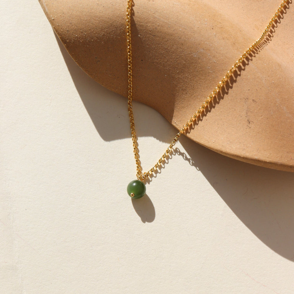 A 14k gold fill small rolo chain featuring a jade ball gemstone. The necklace is displayed on a cream backdrop. 