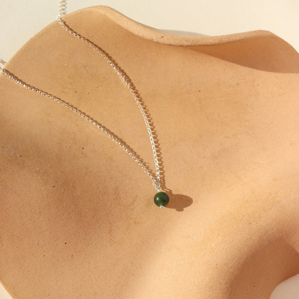 A sterling silver small rolo chain featuring a jade ball gemstone. Necklace is displayed on a orange dish. 