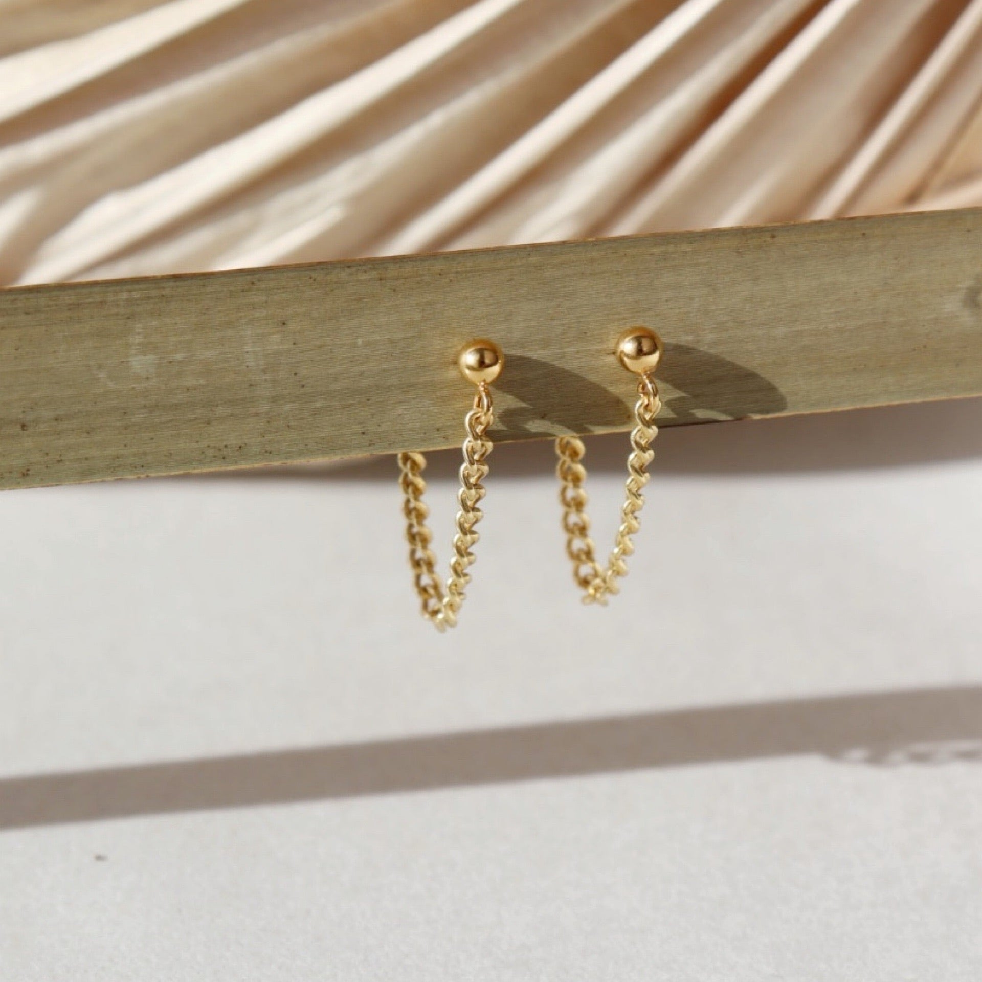 14k gold fill la mer studs placed on a plant leaf.