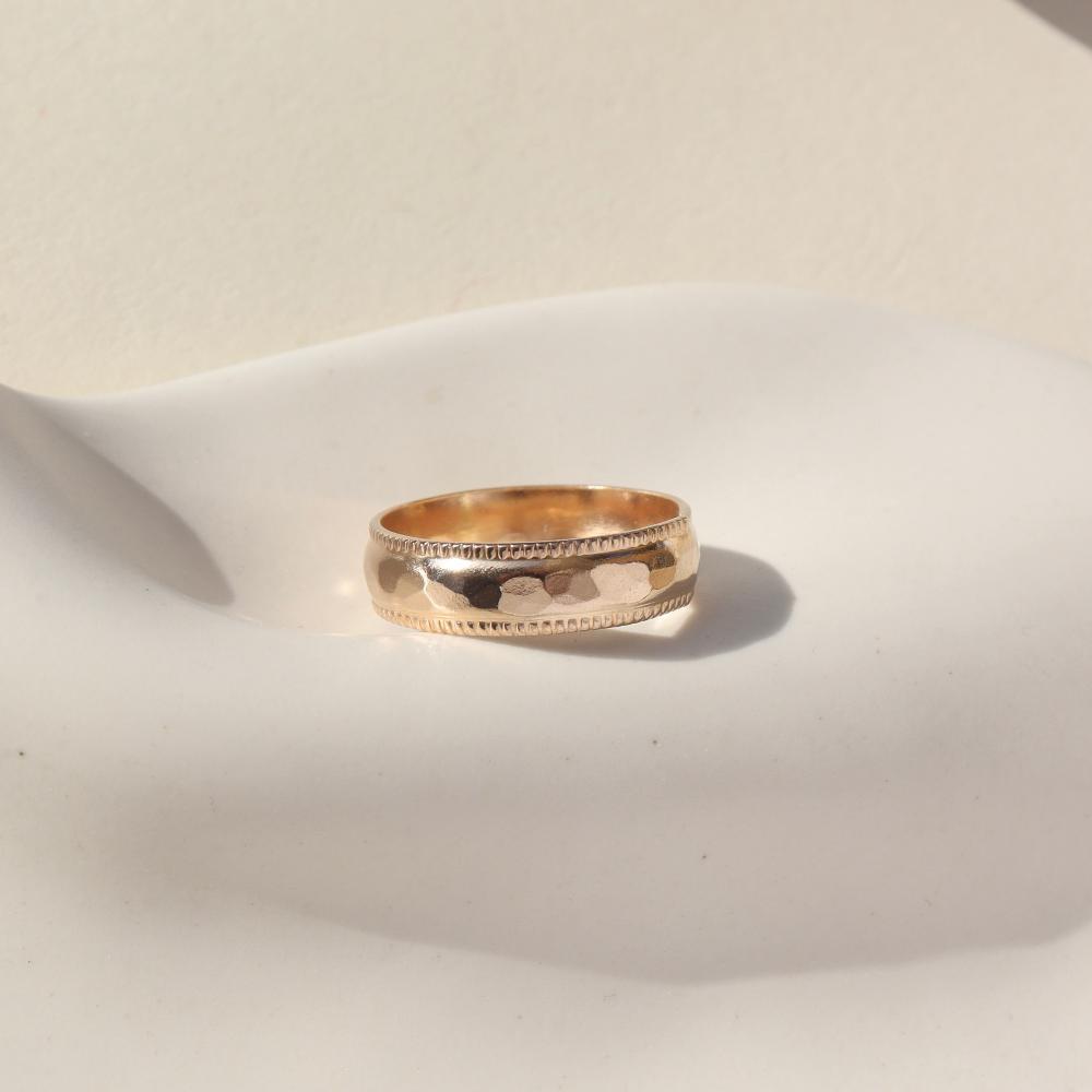 A gold hammered band with rippled edges. Displayed on a small ring dish. 