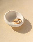 A gold hammered band with rippled edges. Displayed on a small ring dish. 