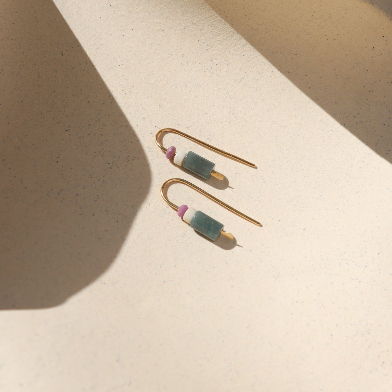gold fill threader earrings with faceted phosphosiderite, fossil jasper, and guatamalan jade on a light dish