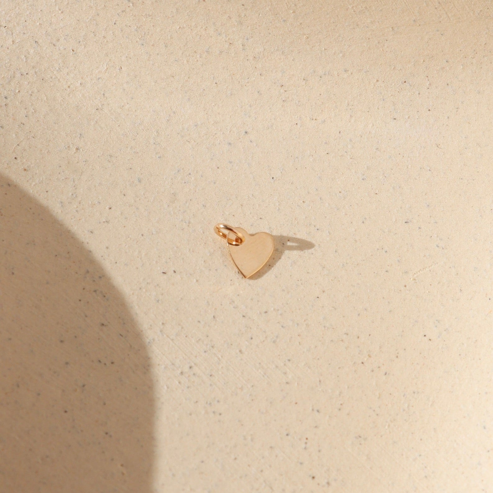 14k gold fill heart charm with jump ring on a light background in the sunlight