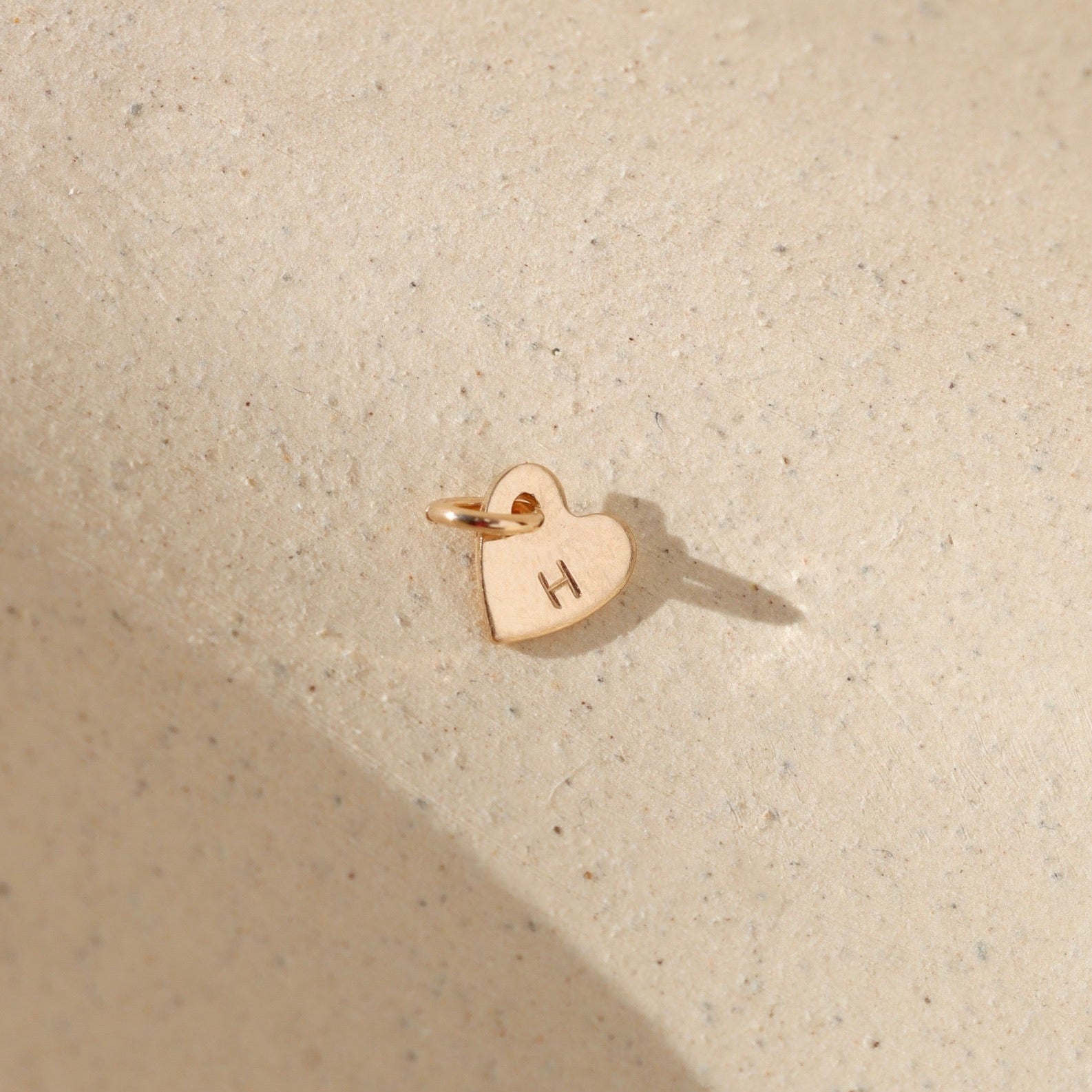 14k gold fill heart charm with jump ring stamped with an 'H' on a light background in the sunlight