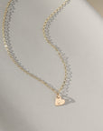 a dainty heart charm with an initial stamped on them, on a necklace chain, photographed on a ceramic dish