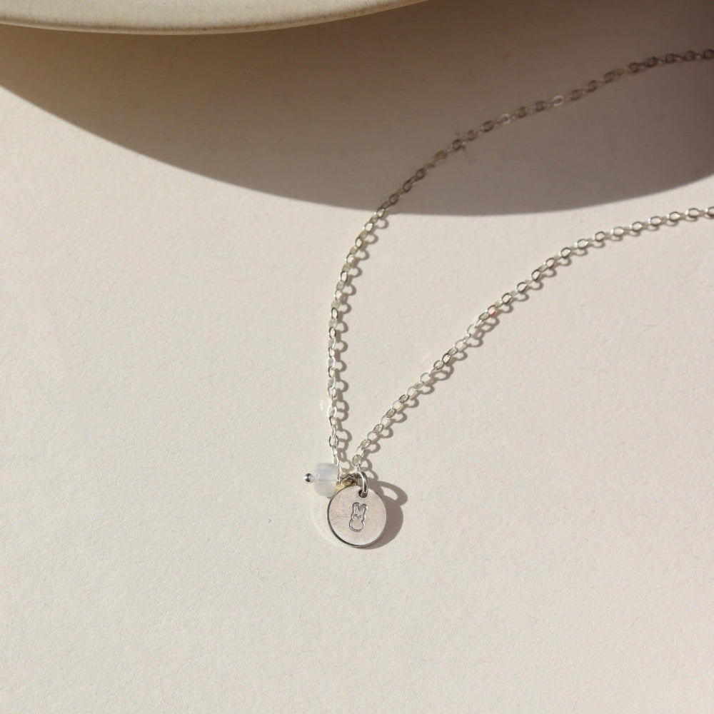 A sterling silver simple chain with a stamped disc with a small bunny, paired with a small opal wire wrapped gemstone. 