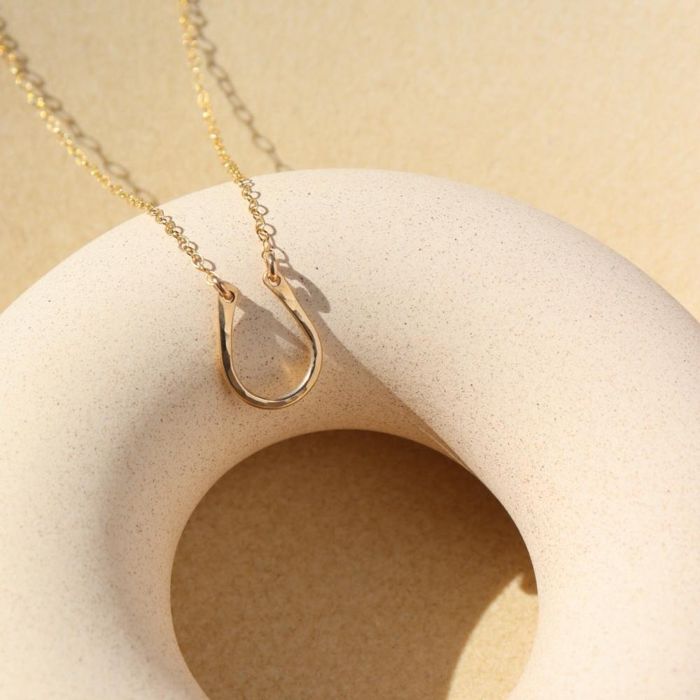 14k gold fill Lucky Charm Necklace. This Necklace features a horseshoe shape with hammering on one side. The horseshoe meaning lucky is connected with the simple chain.