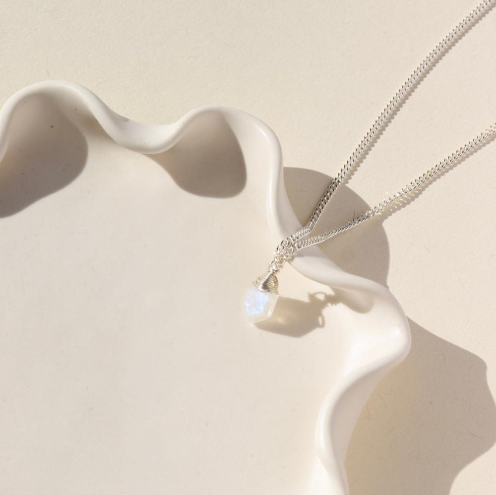 Delicate silver curb chain, with moonstone slice gemstone. Displayed on a cream backdrop. 