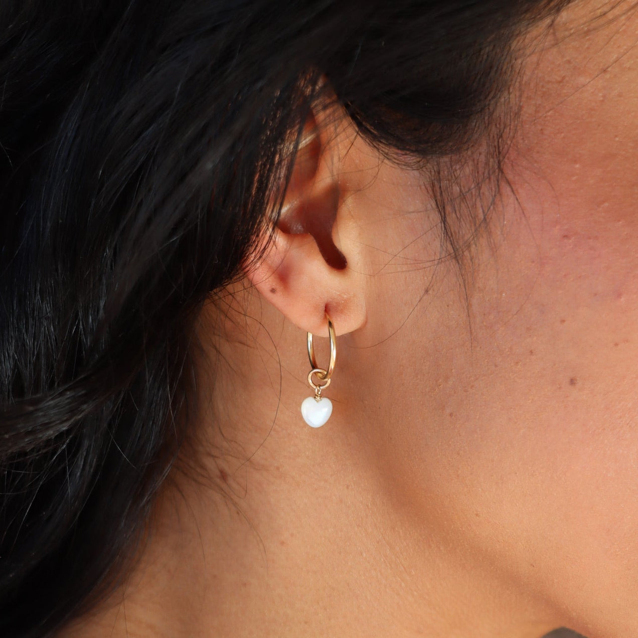 model wearing mother of pearl heart charm in 14k gold fill on 14k gold fill simple hoop