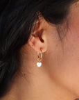 model wearing mother of pearl heart charm in 14k gold fill on 14k gold fill simple hoop