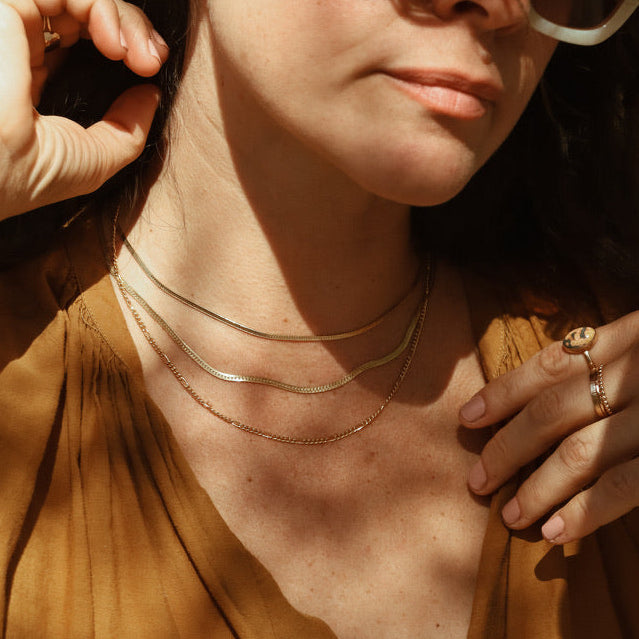 model wearing 2 14k gold fill herringbone chain necklaces with a figaro chain necklace