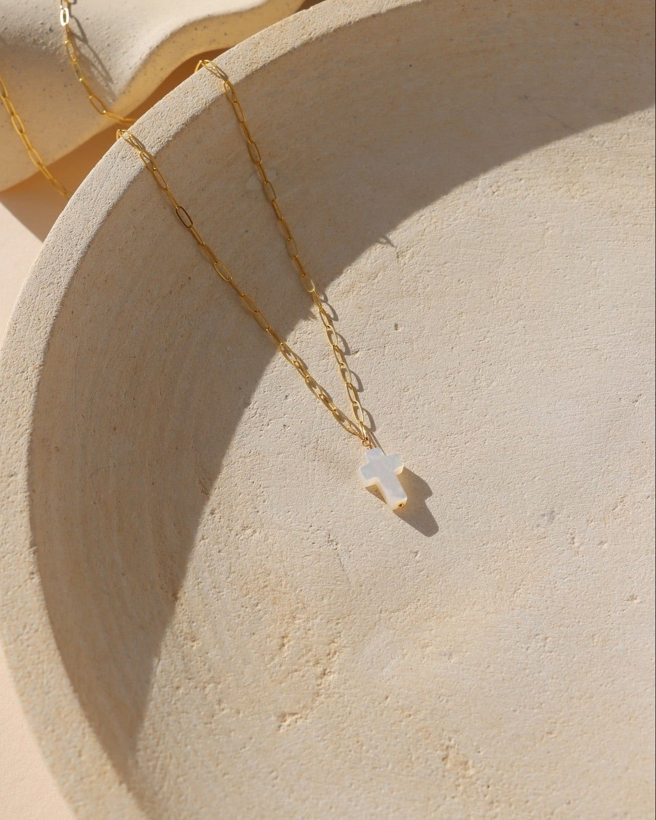 14k gold fill paperclip chain with a mother of pearl cross bead pendant on a light plate