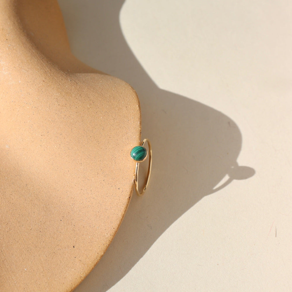 A 14k gold fill skinny band featuring a 5mm malachite stone set in a gold bezel. The 5mm Malachite Ring is displayed on a cream dish. 