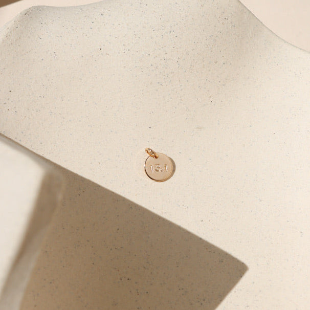 14k gold fill round disc with marathon miles hand stamped on it on a light dish