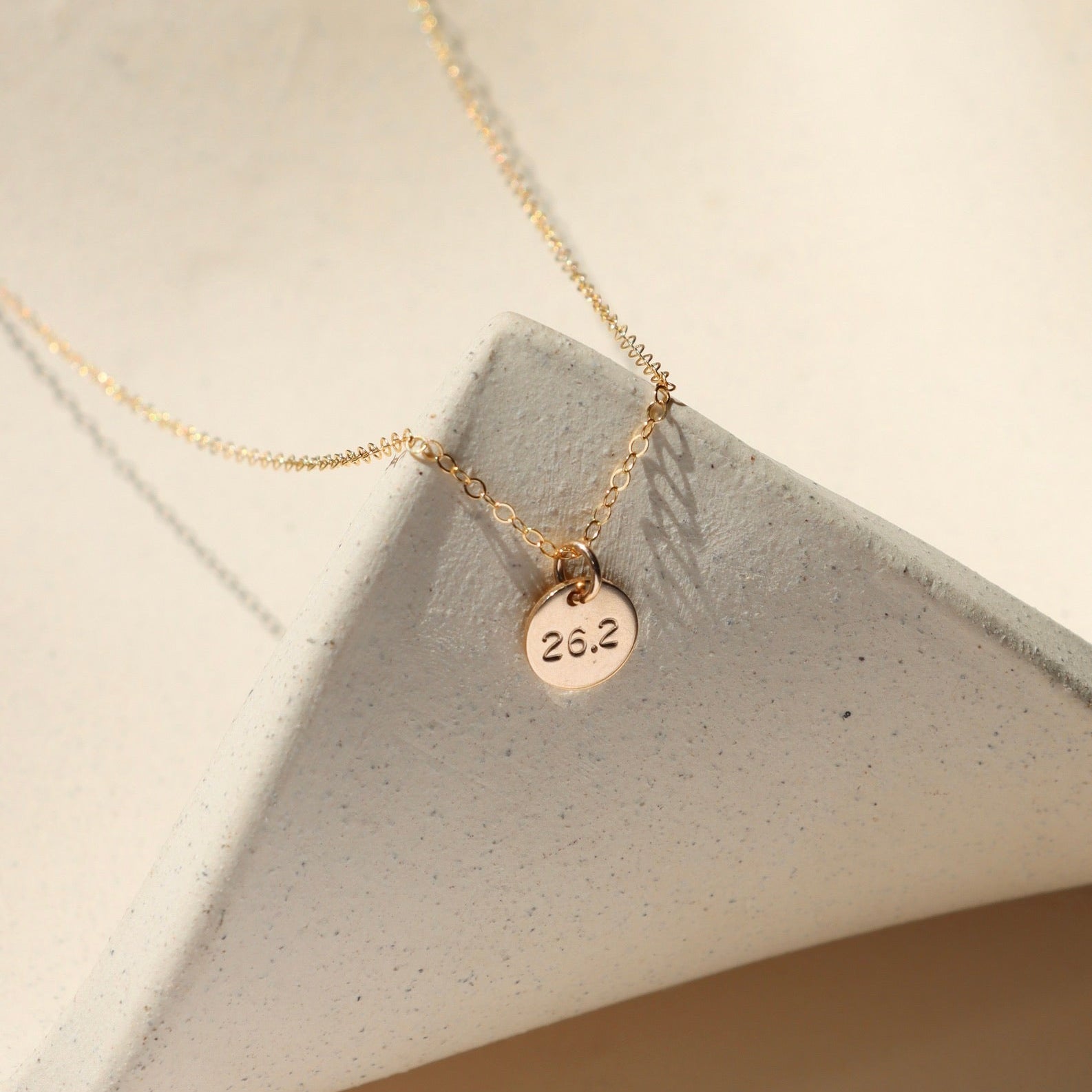 14k gold fill hand stamped round disc charm on a delicate chain necklace on a light surface