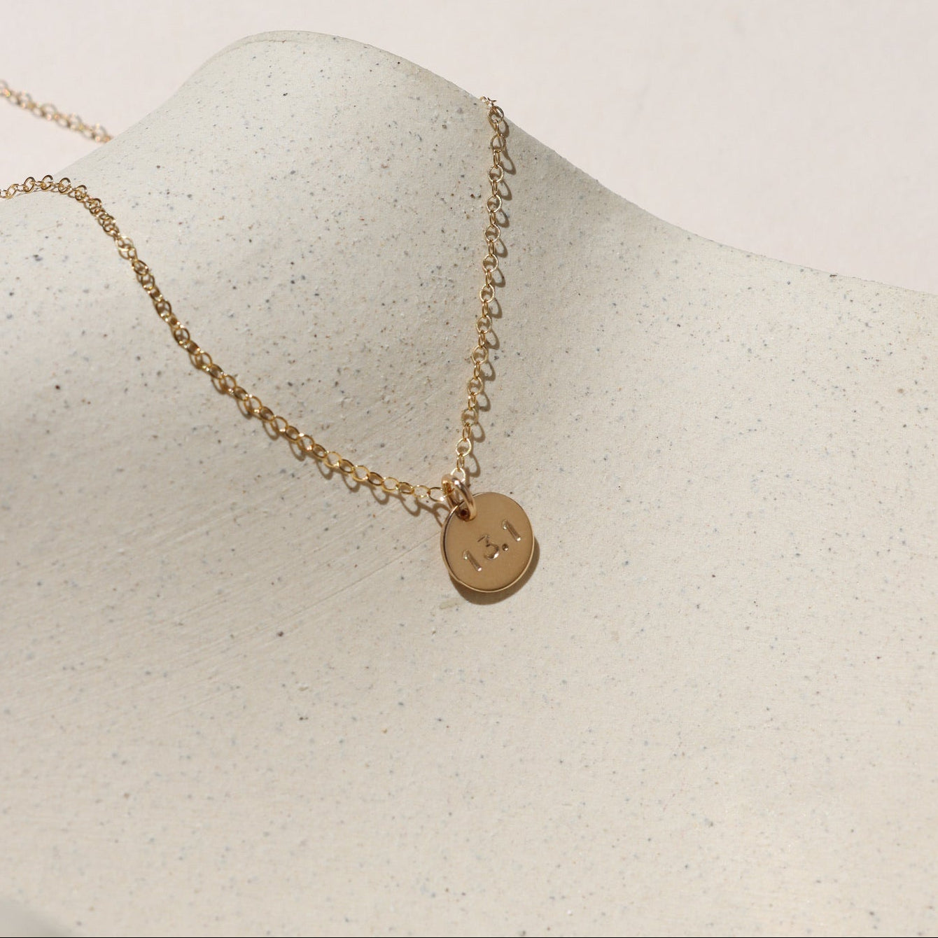 14k gold fill hand stamped round disc charm on a delicate chain necklace on a light surface