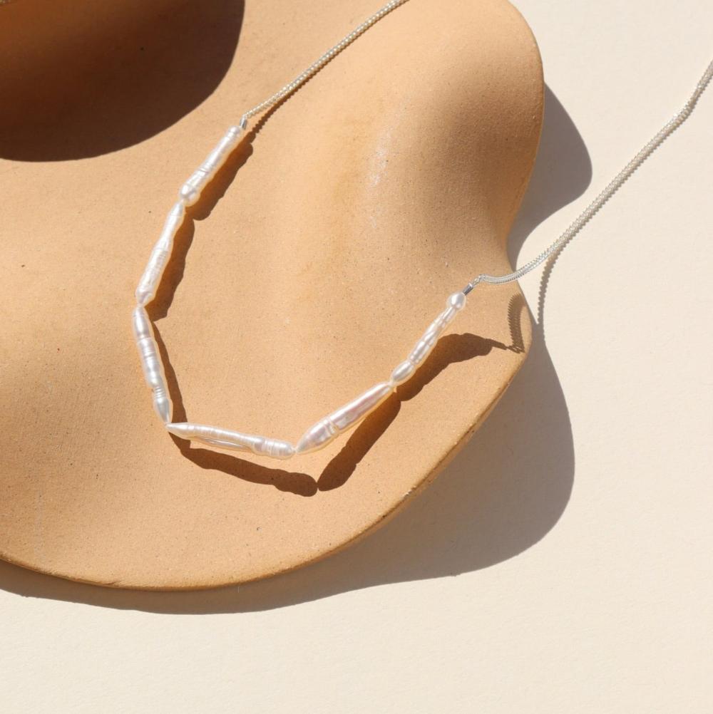 A silver curb chain with six elongated pearl. Displayed on a tan dish with a cream backdrop. 