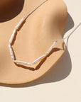 Maren Pearl Necklace in Sterling silver laid on a tan plate in the sunlight