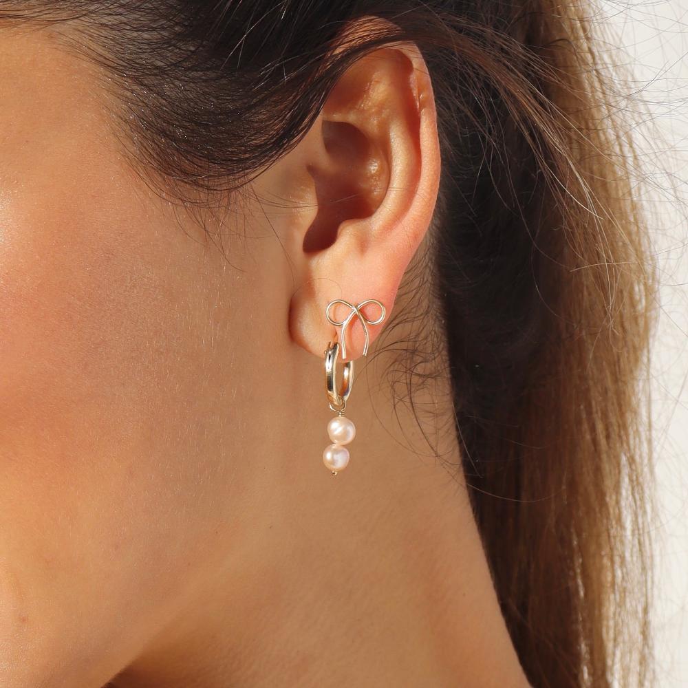model wearing 14k gold fill hand shaped bow stud earrings with hoop earrings that have pearl charms