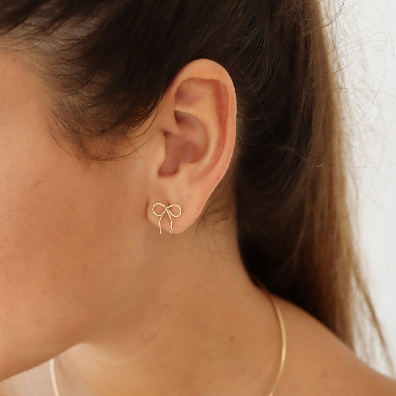 model wearing 14k gold fill hand shaped bow stud earrings 
