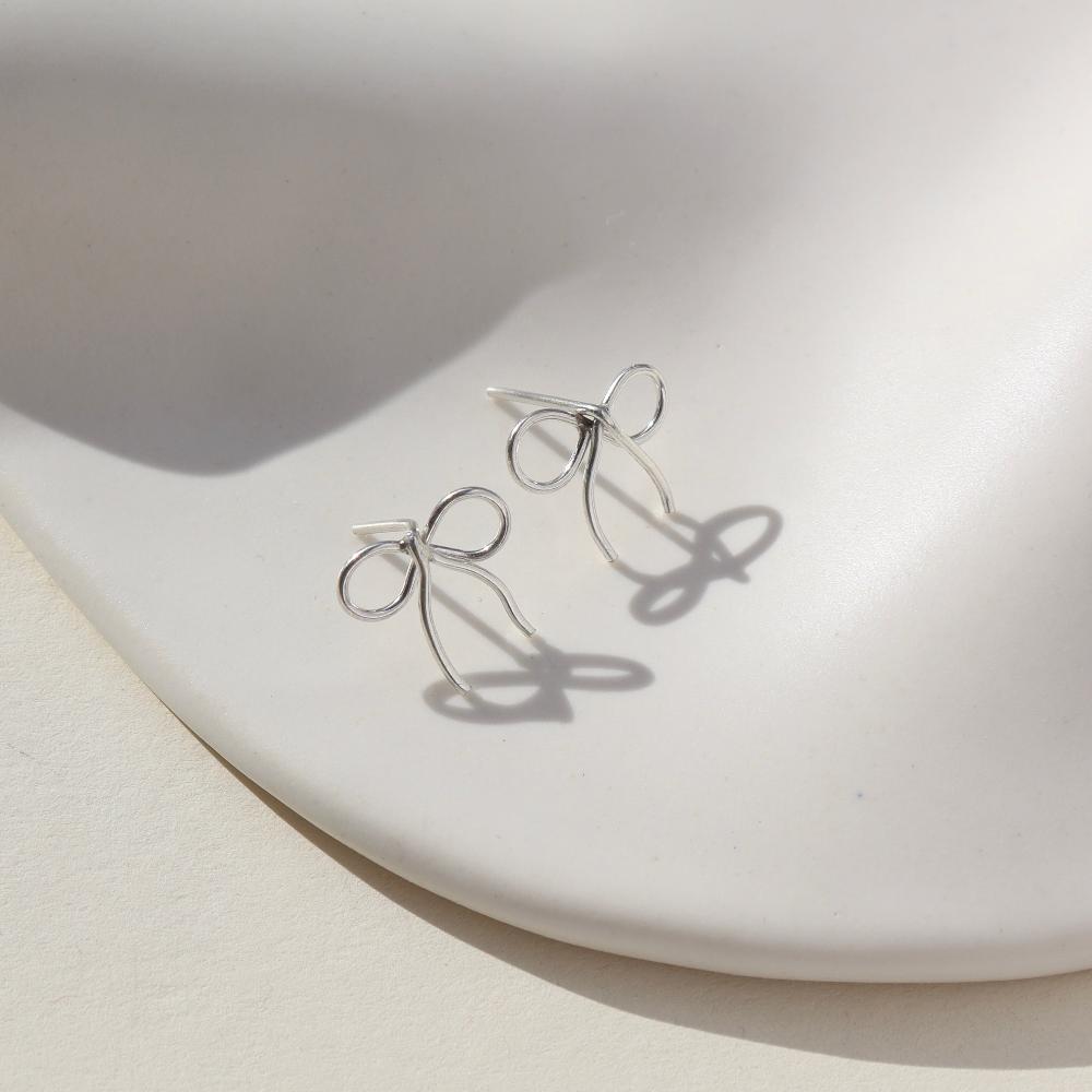 sterling silver hand shaped bow stud earrings on a light dish