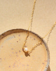 14k gold fill Mini Pearl Necklace laid on a tan bowl in the sunlight. This Necklace features a mini pearl with connected by the simple chain.