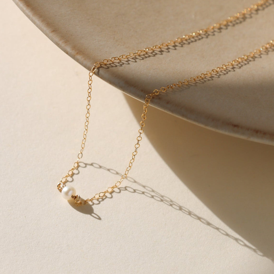 Gold necklace with a small pendant on a beige surface