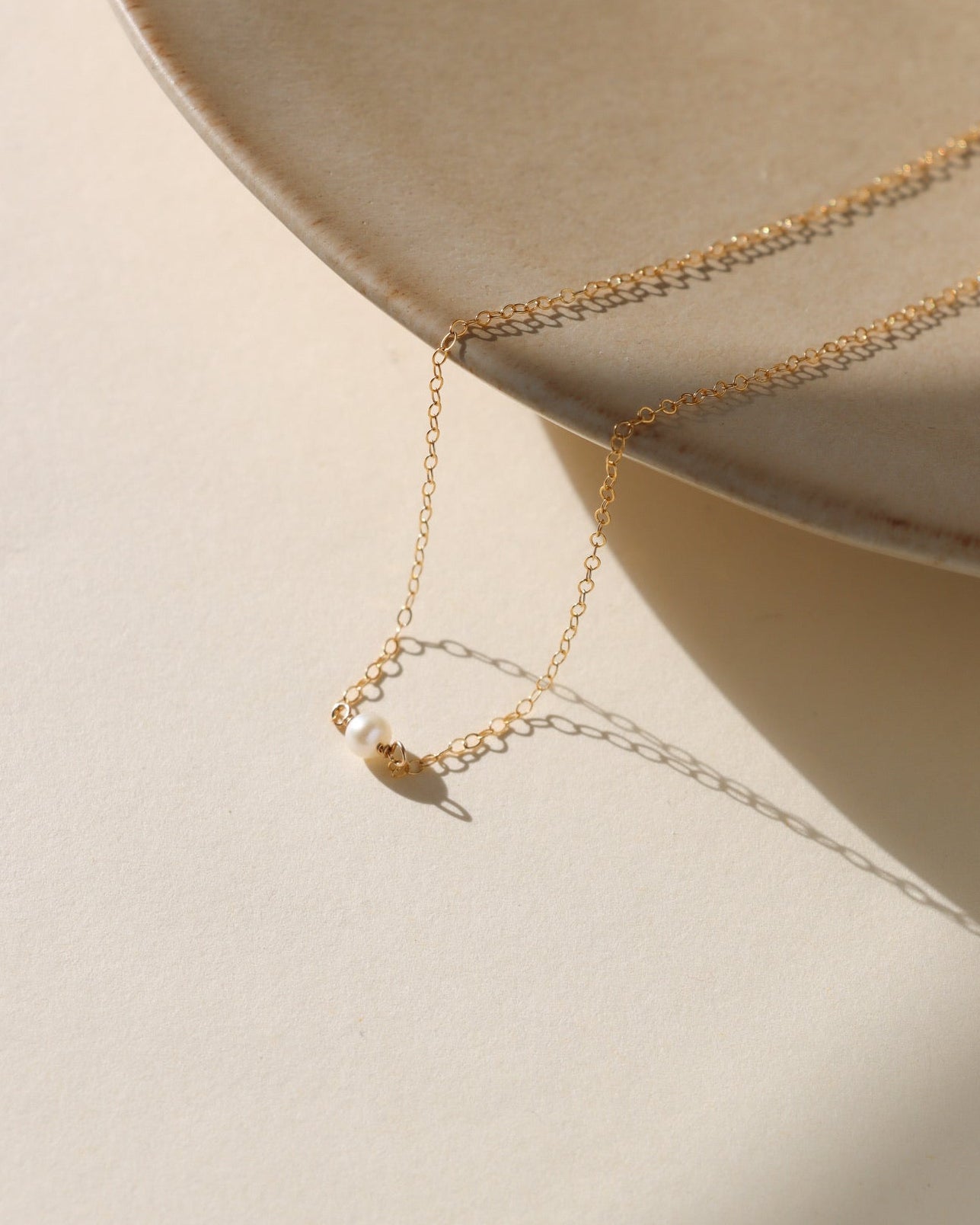 14k gold fill necklace with a small pearl on a beige surface