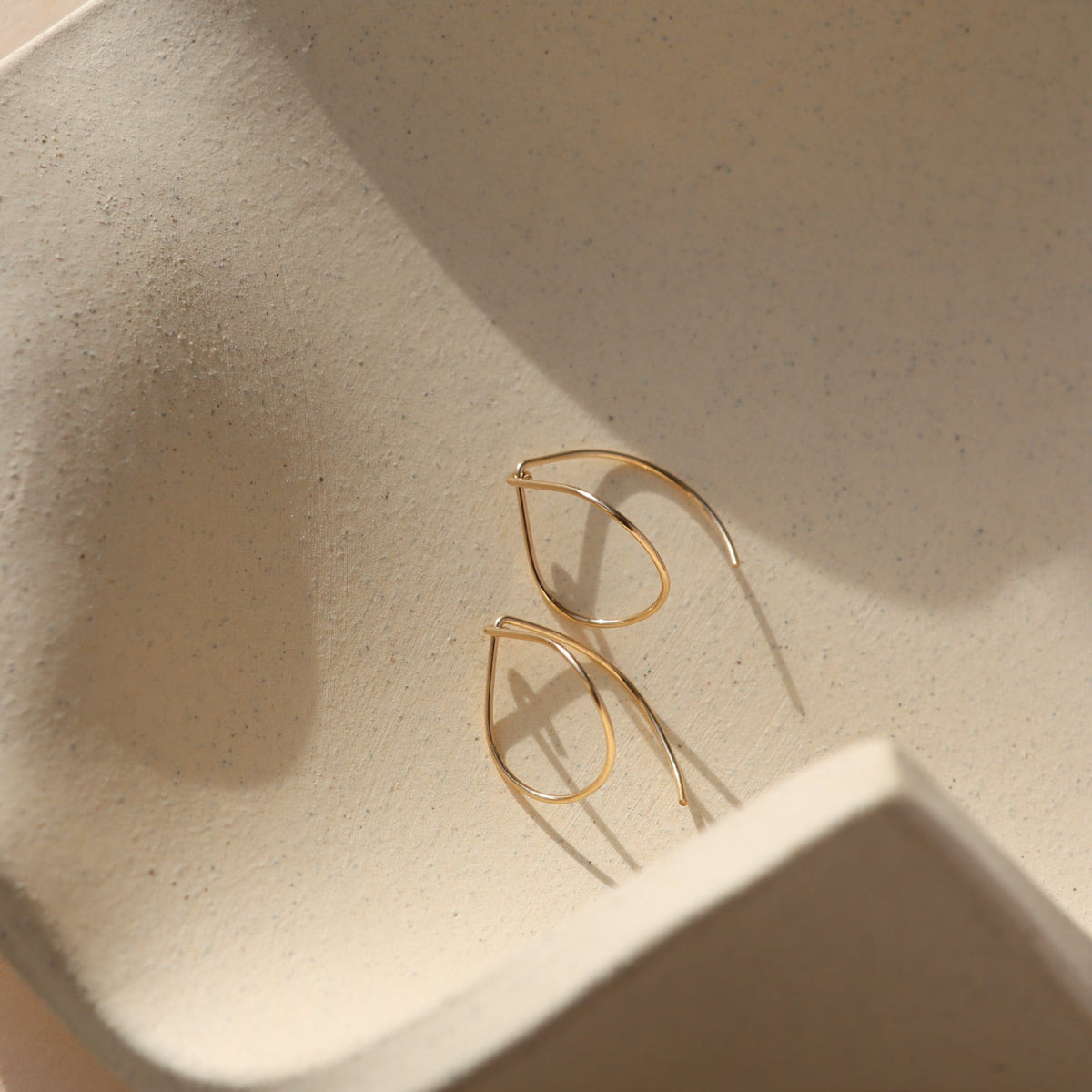 14k gold fill teardrop shaped earrings on a light textured dish