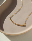 14k gold fill Minimal Necklace placed on a tan plate in the sunlight. This Necklace features a small bar about two inches long and connected by our simple chain.