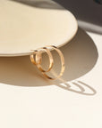 A thick hammered hoop offered in three sizes (small, medium, and large) displayed hanging on a tan dish. 