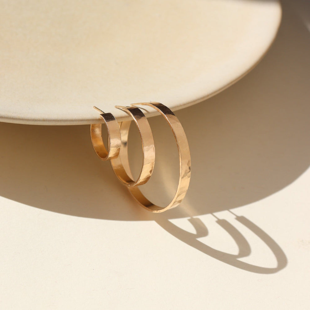 A thick hammered hoop offered in three sizes (small, medium, and large) displayed hanging on a tan dish. 