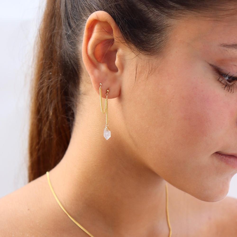 Model wearing the gold lumi chain stud. Earring features gold curb chain with a moonstone dangling from the end. Earrings are made for a double piercing. 