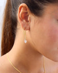 Model wearing the gold lumi chain stud. Earring features gold curb chain with a moonstone dangling from the end. Earrings are made for a double piercing. 