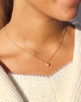 Brunette model wearing the pink pearl necklace. This necklace features a dainty gold chain with a small pink pearl hanging at the end. 