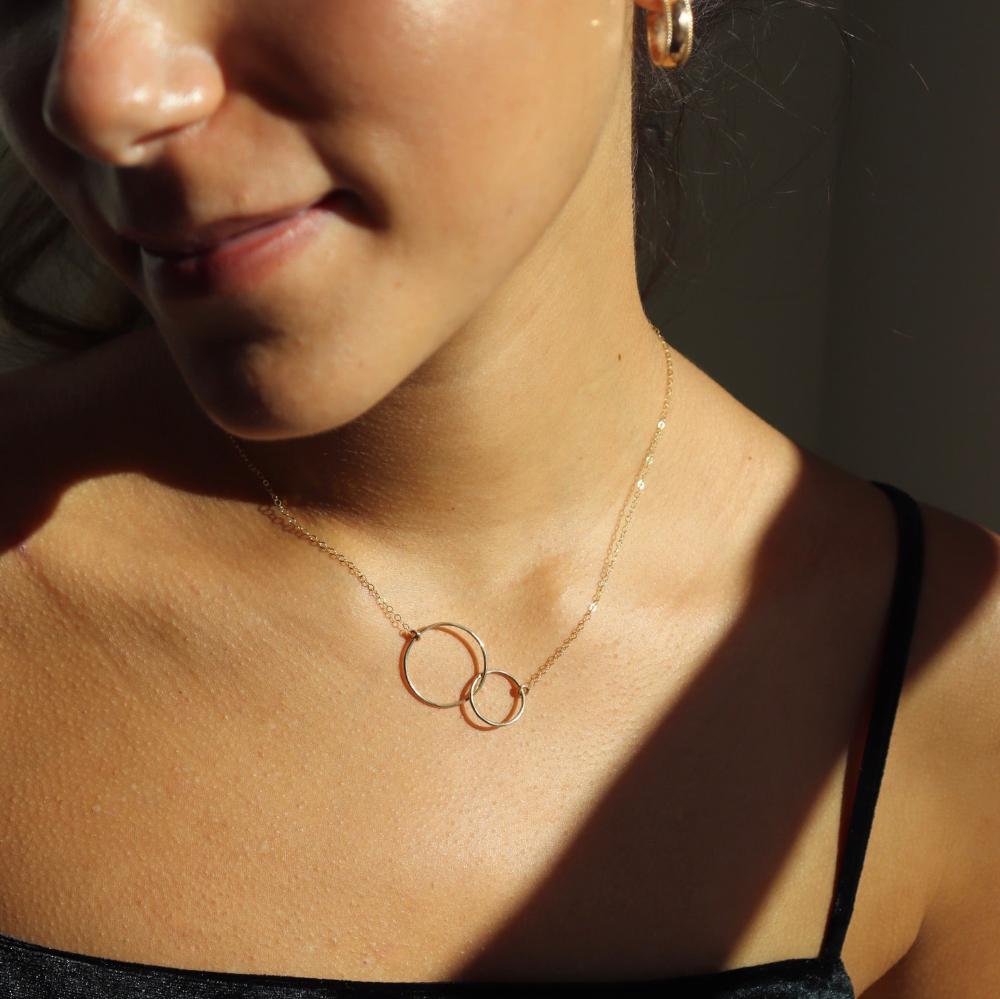 Brunette model wearing the unity necklace. This necklace features a dainty gold chain with a large and small circle connecting in the center. 