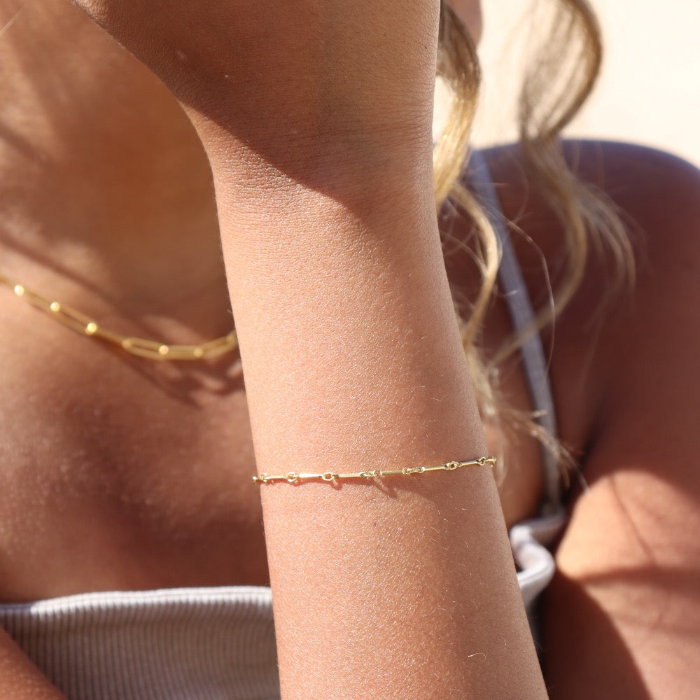 Model wearing 14k gold fill dot + dash bracelet. This is a gold bar link chain. Model is wearing a light purple tank top. 